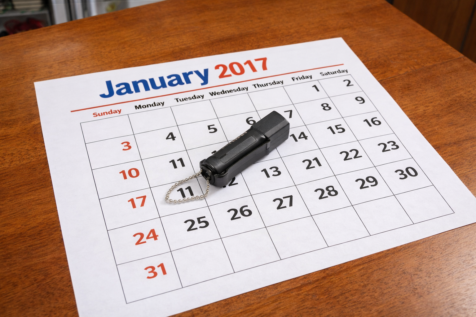 A January of 2017 calendar page lying on a table with a small black canister of pepper spray lying flat near the center of the page